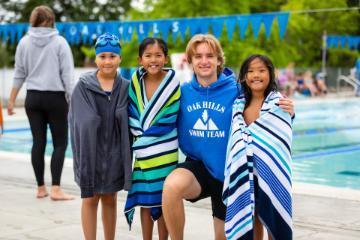 Four people by a pool with towels, wearing swimming attire.