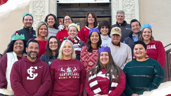 18 smiling people in holiday themed outfits outside Bannan Alumni House