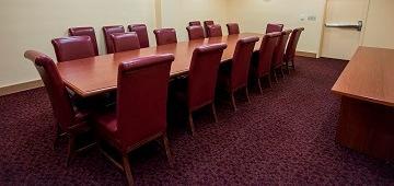 A conference room with a large table and red chairs.