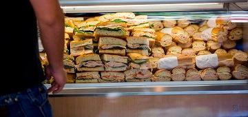 A person standing near a display of various sandwiches.