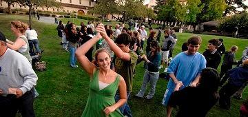 Students dancing outdoors at an event with other attendees in the background.
