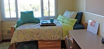 A tidy and inviting dorm room with a bed and study desk.