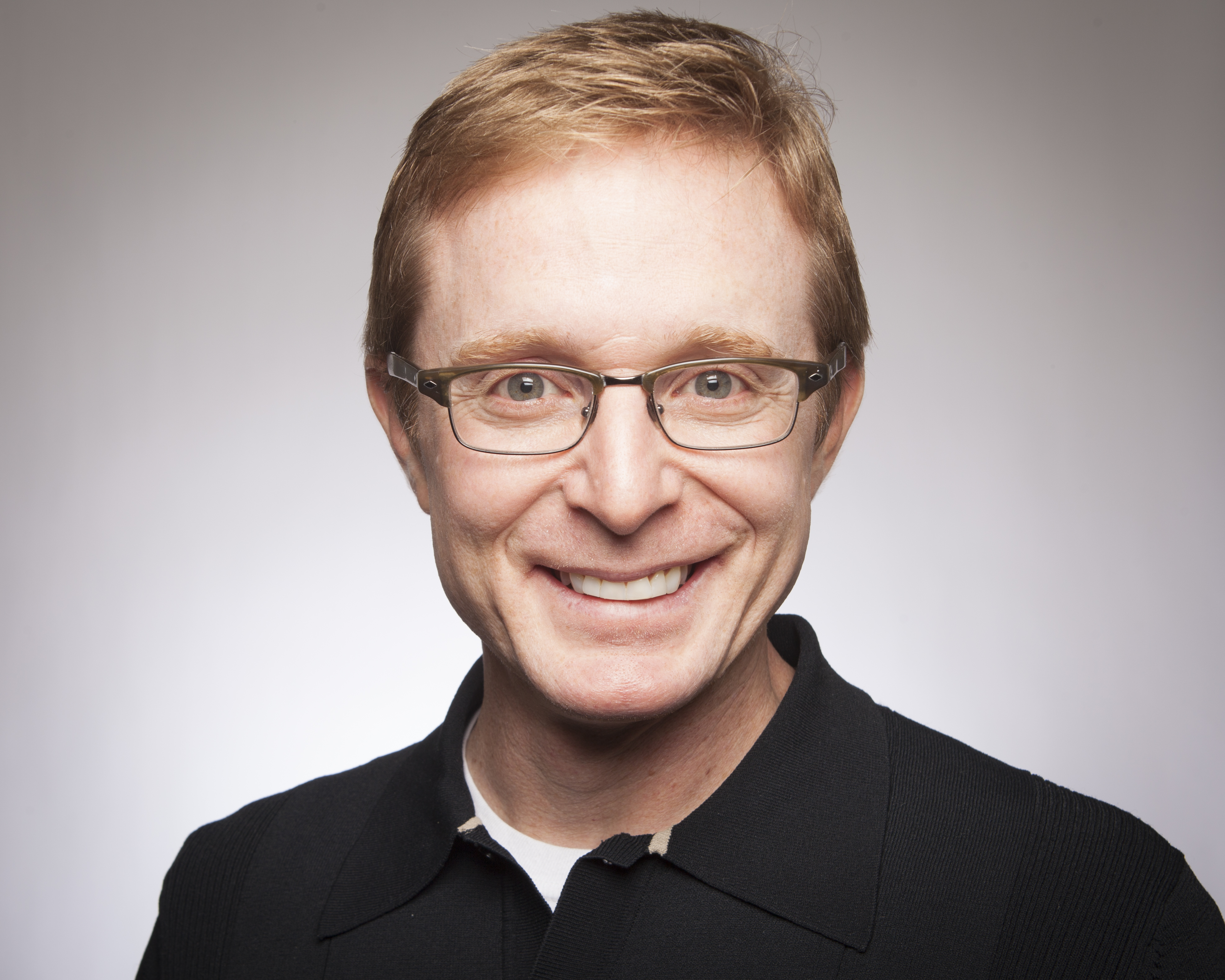 A smiling person wearing glasses against a plain background.