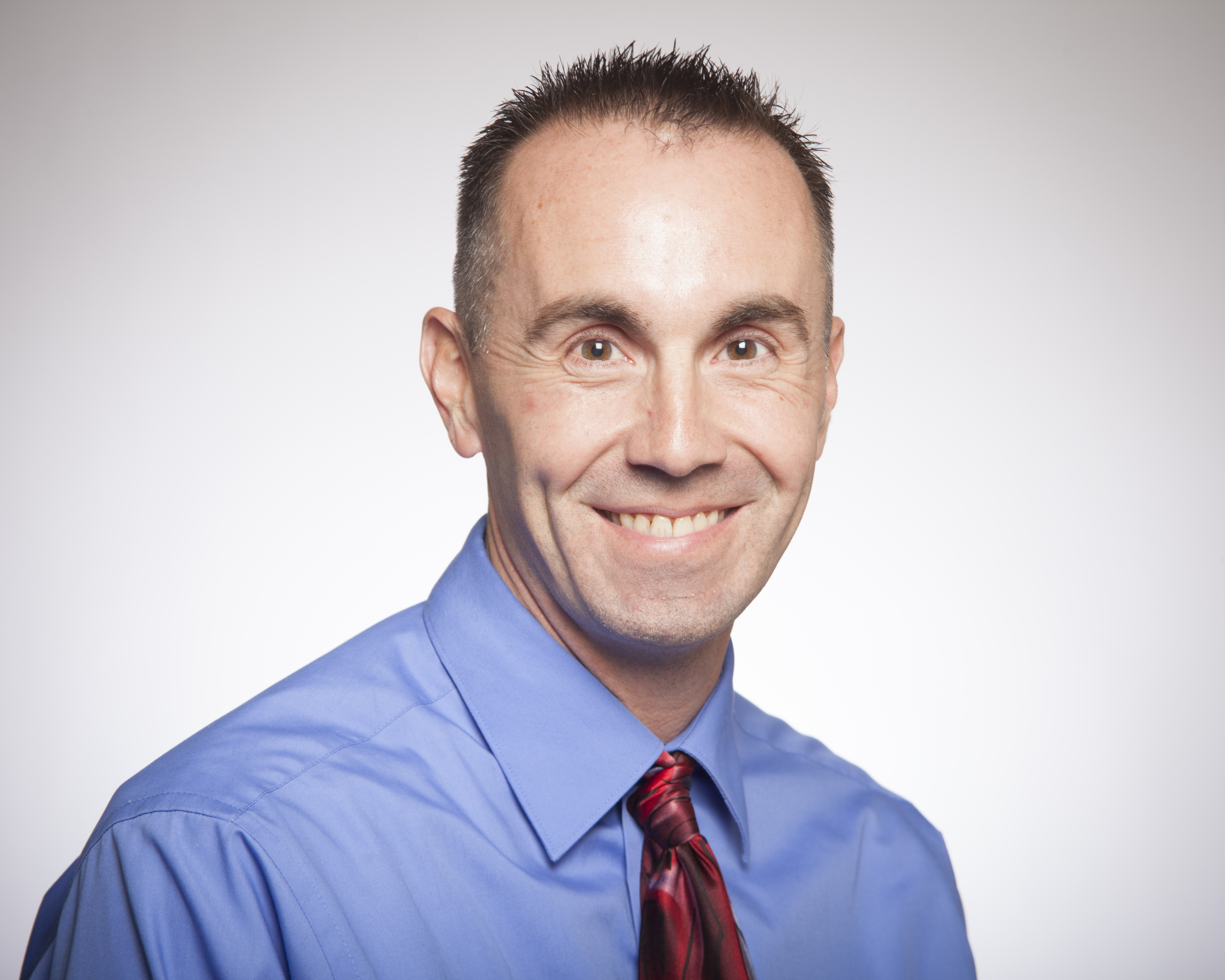 A person wearing a blue shirt and red tie smiling.