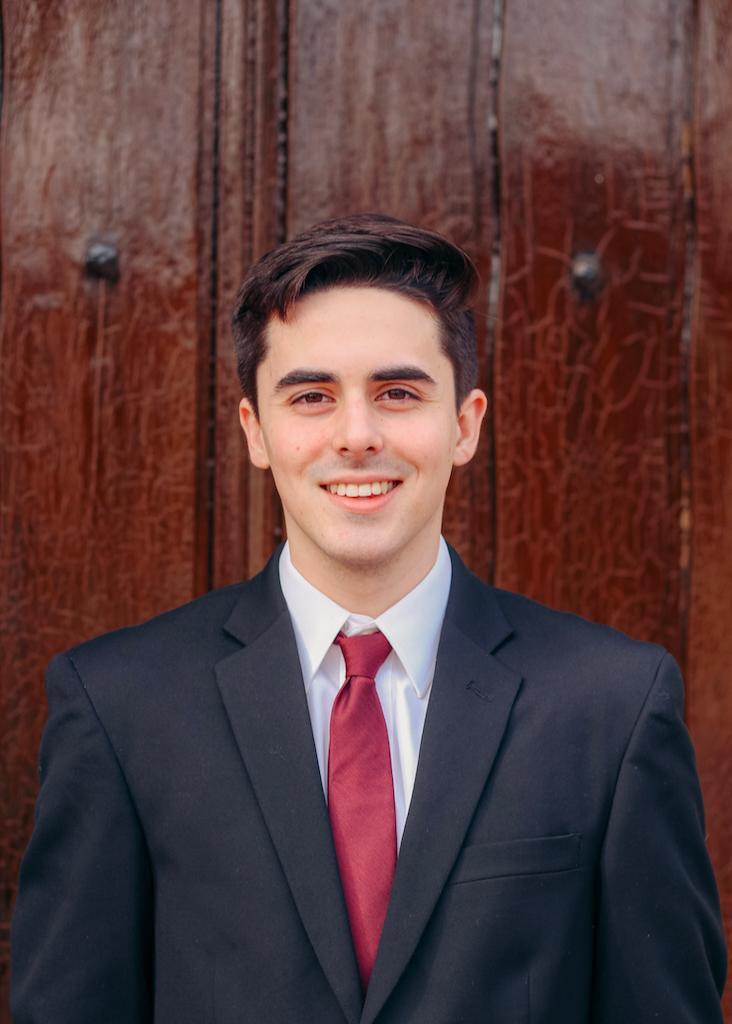 A person in a suit with a red tie, smiling.