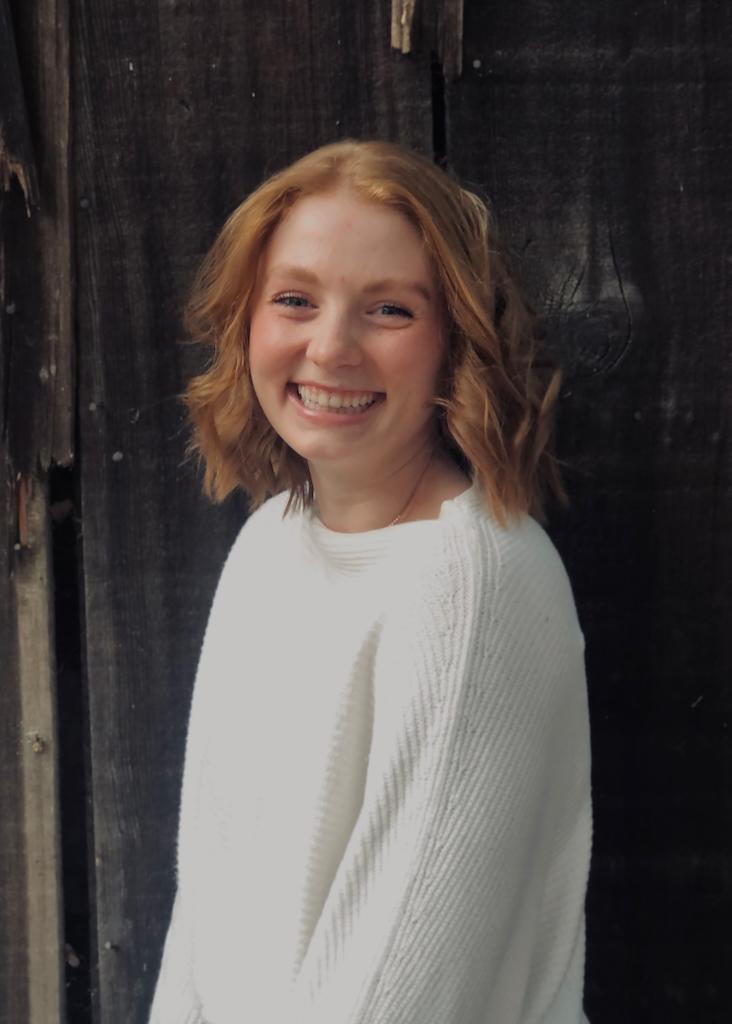 A person in a white sweater smiles in front of a dark background.