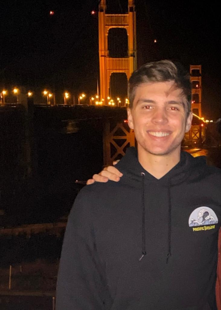 Person smiling in front of the Golden Gate Bridge at night.