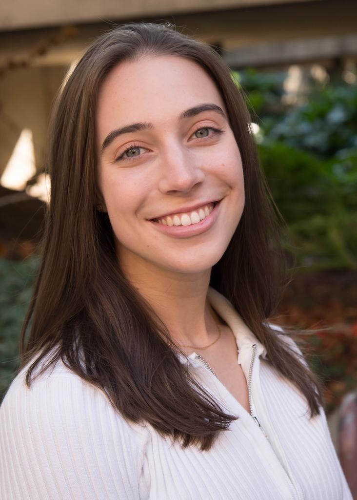 Smiling person posing outdoors with greenery in the background.