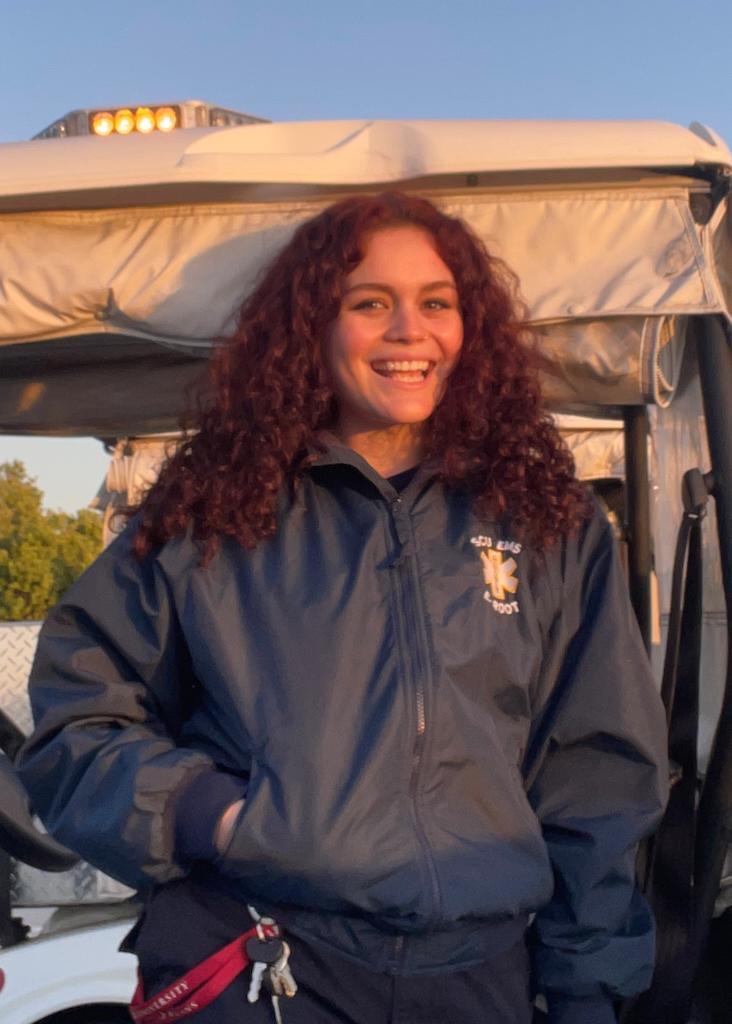 Woman in a dark jacket stands next to a vehicle, smiling.