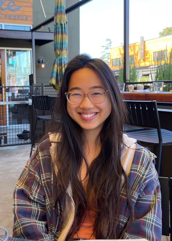 A person smiling while sitting inside a cafe.