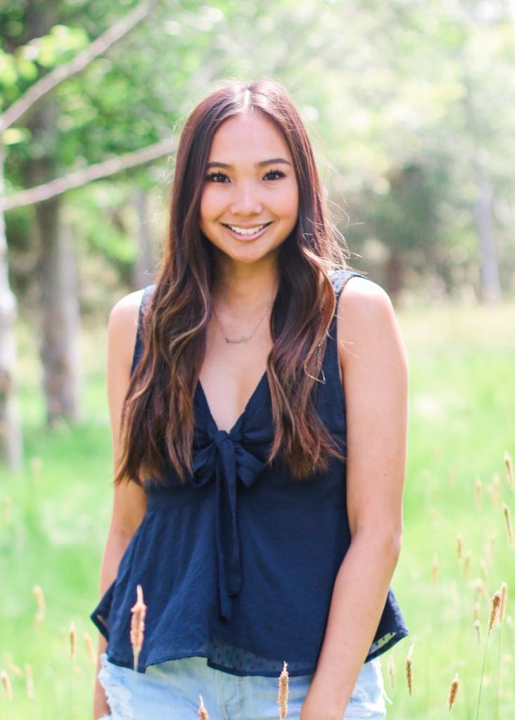 A smiling person standing outdoors in a grassy area.