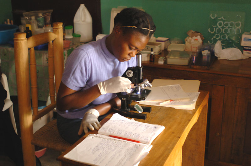 A woman using a microscope at a research table with books. image link to story