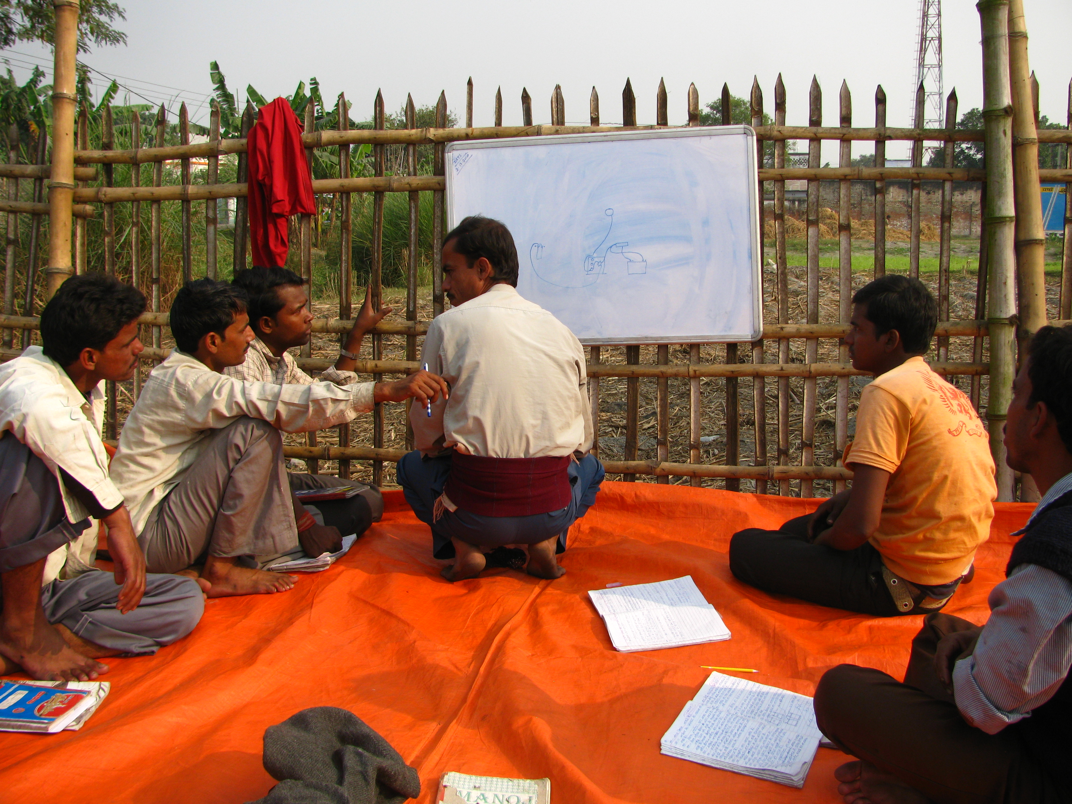 People sitting on a tarp, brainstorming in front of a whiteboard outdoors. image link to story