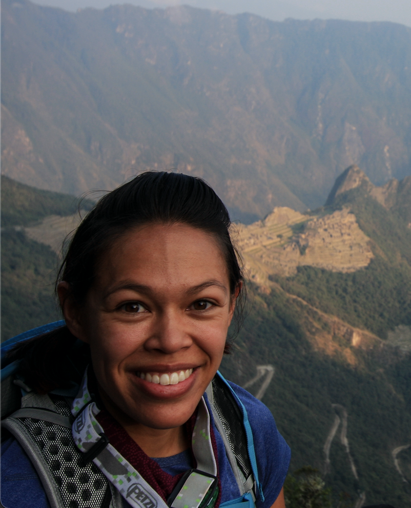 A person smiling with a mountain landscape in the background.