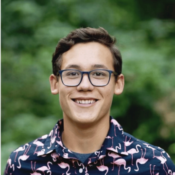 A person wearing glasses and a patterned shirt smiles.