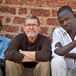 Three people sitting against a brick wall background.