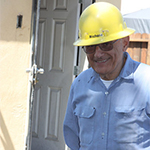 A person in a hard hat and blue shirt standing near a building.