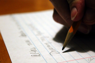 Alt text: Hand holding a pen, writing on a lined paper with lists.