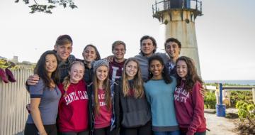 A group of people posing in front of a lighthouse with smiles. 

