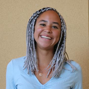 A person smiling while wearing a light blue top.