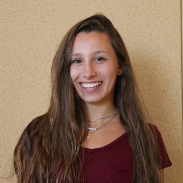 A person smiling in front of a tan wall.