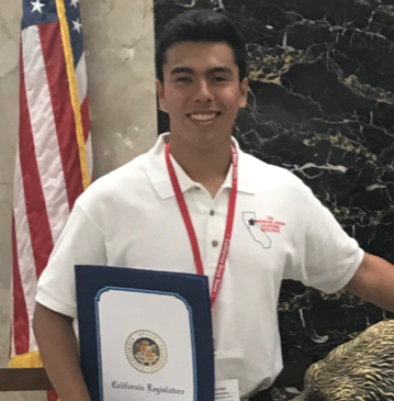 A person holding a certificate, standing in front of the US flag.