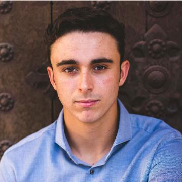 A person in a blue shirt sitting in front of a wooden background.