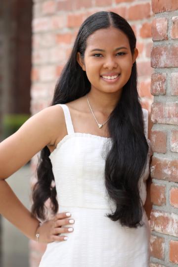 A person smiling in a white outfit against a brick wall.