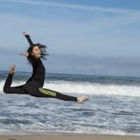 A person performing a leap on the beach near the ocean.