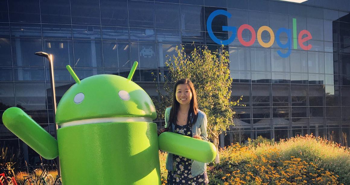 Person posing with large Android mascot at Google campus. image link to story