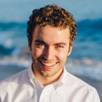 Smiling person in a white shirt with a beach in the background.