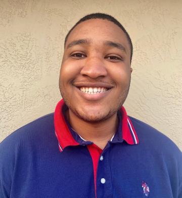 A person smiling in a blue shirt with a red collar against a beige background.