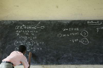 A person writing equations on a large chalkboard.