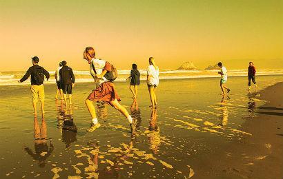 People walking on a beach at sunset with a yellow sky.