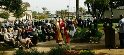 A priest blessing a garden while people observe.