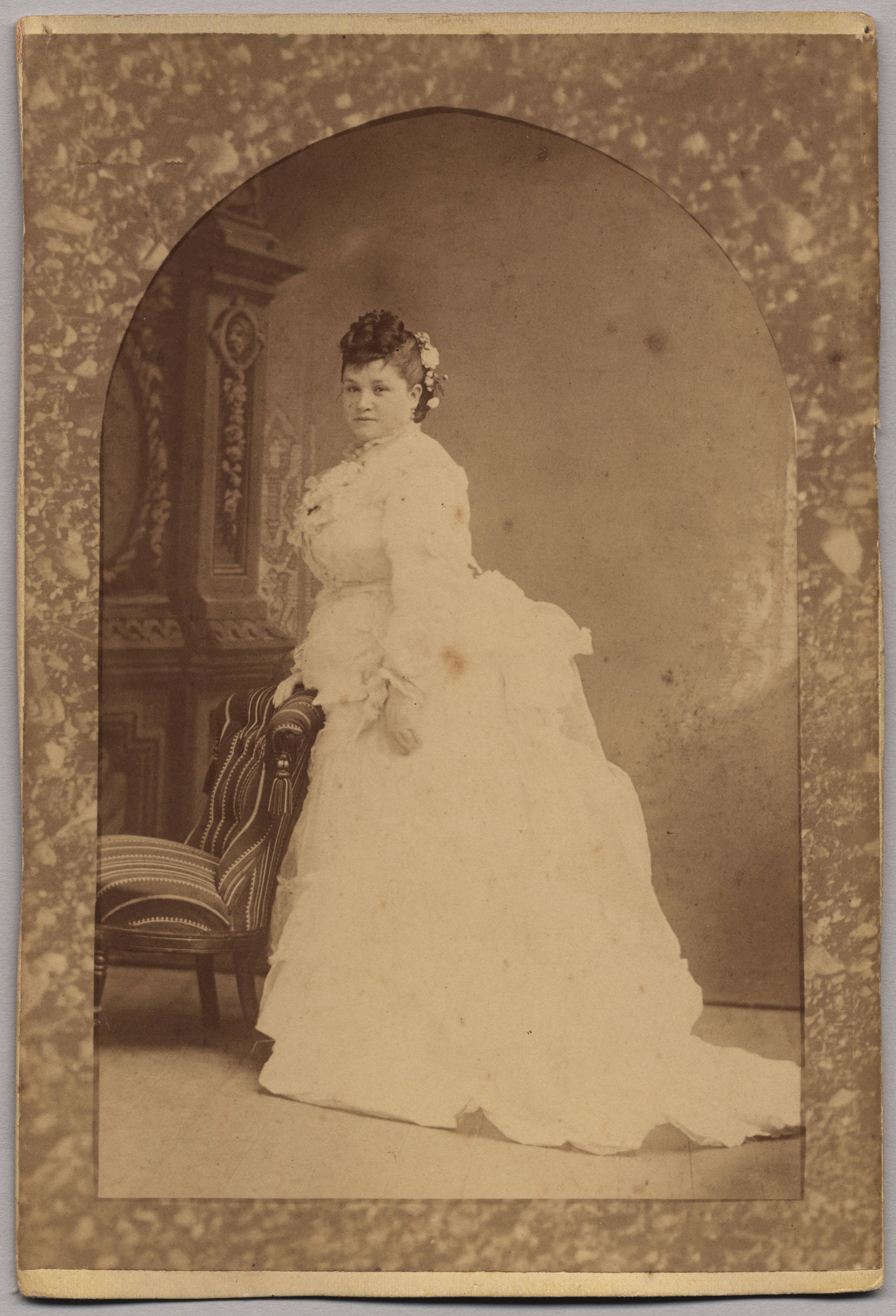 A sepia-toned portrait of a woman in a long white dress from around 1870.