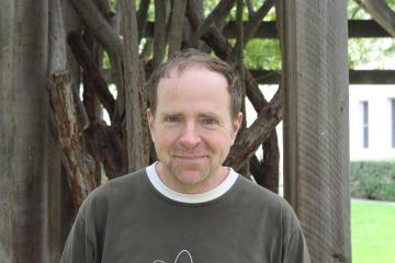 A man standing in front of wooden beams and greenery outside.