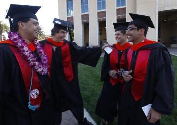 Four graduates in caps and gowns conversing outside a building.