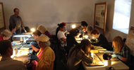 People participating in an archaeology program, examining artifacts at tables with magnifying lamps.