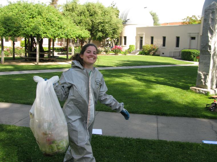 student smiling in a hazmat suit while carrying trash at a waste characterization