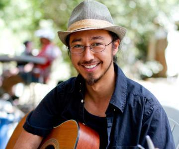 Man smiling and holding a guitar outdoors.