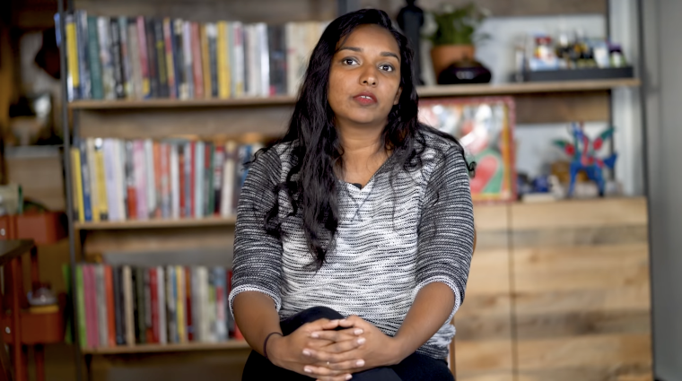 Thanu Yakupitiyage from 350.org sits speaking with a bookshelf and table in the background