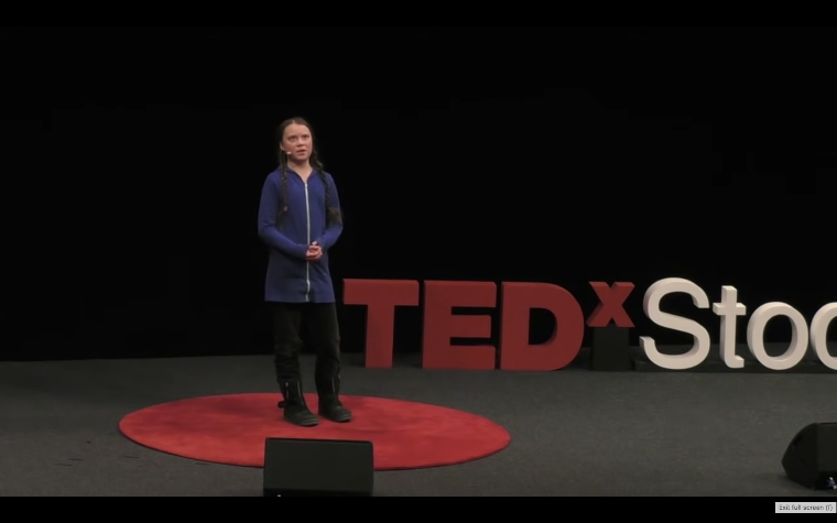 Climate activist Greta Thunberg speaks on stage with the words 