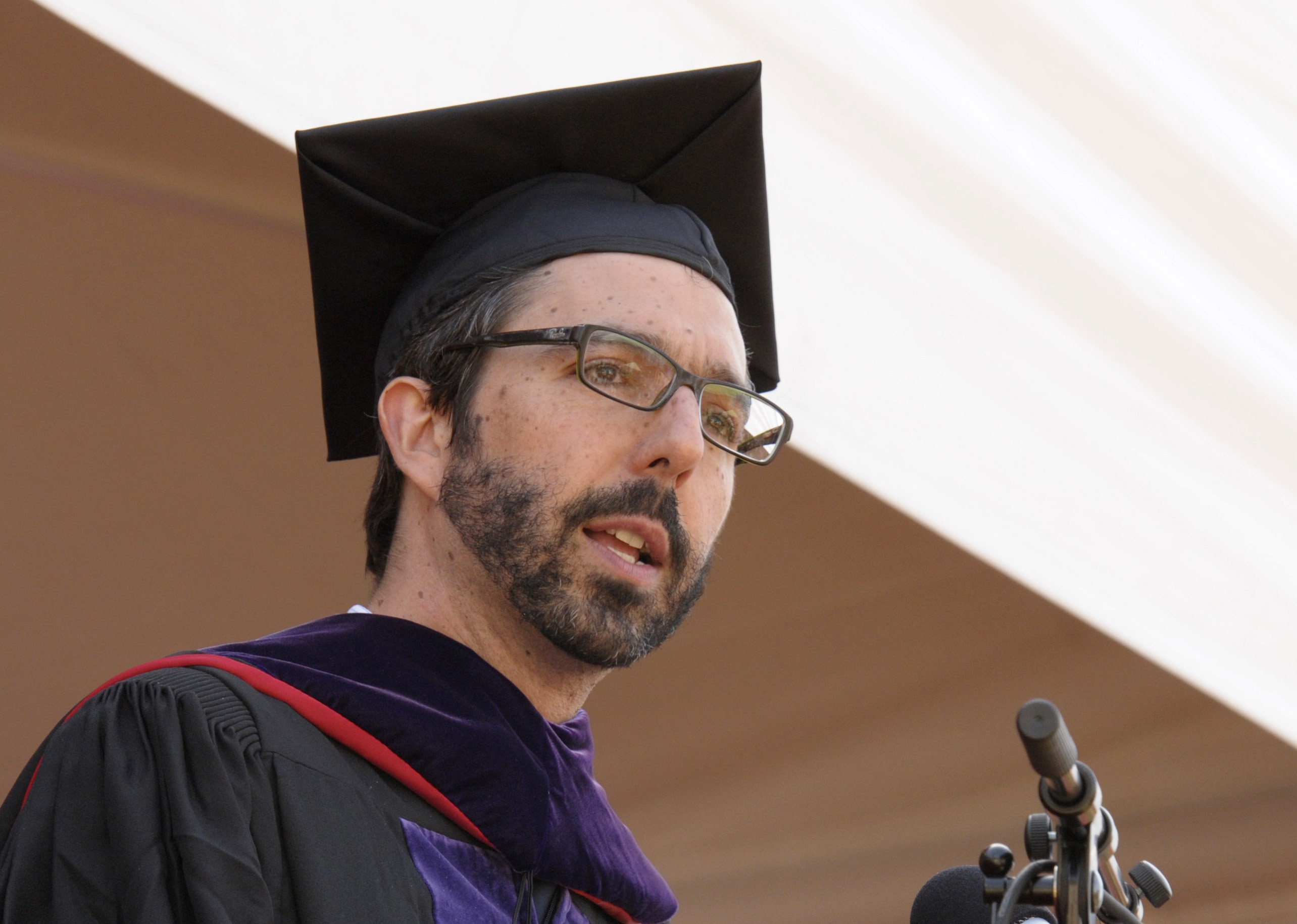 A person in graduation attire speaking into a microphone. image link to story