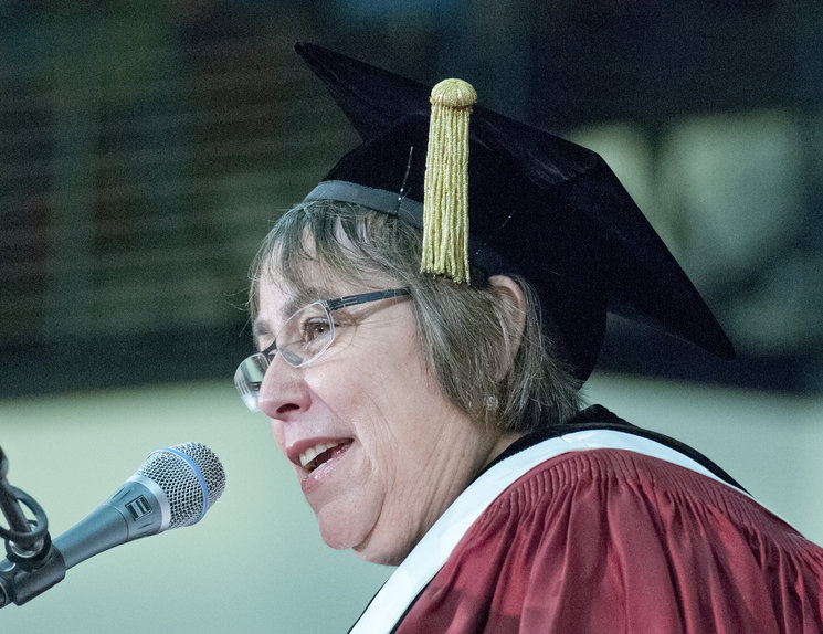 A person in graduation attire speaking at a microphone. image link to story