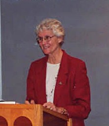 A person in a red jacket speaks at a podium.