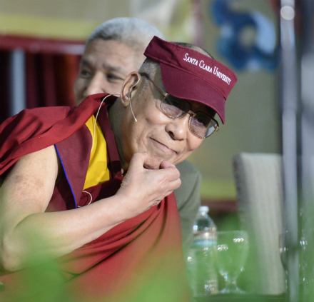 The Dalai Lama smiling, wearing traditional robes and a red visor. image link to story