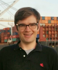 Person smiling outdoors with buildings in the background.