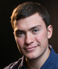 A person smiling against a dark background.