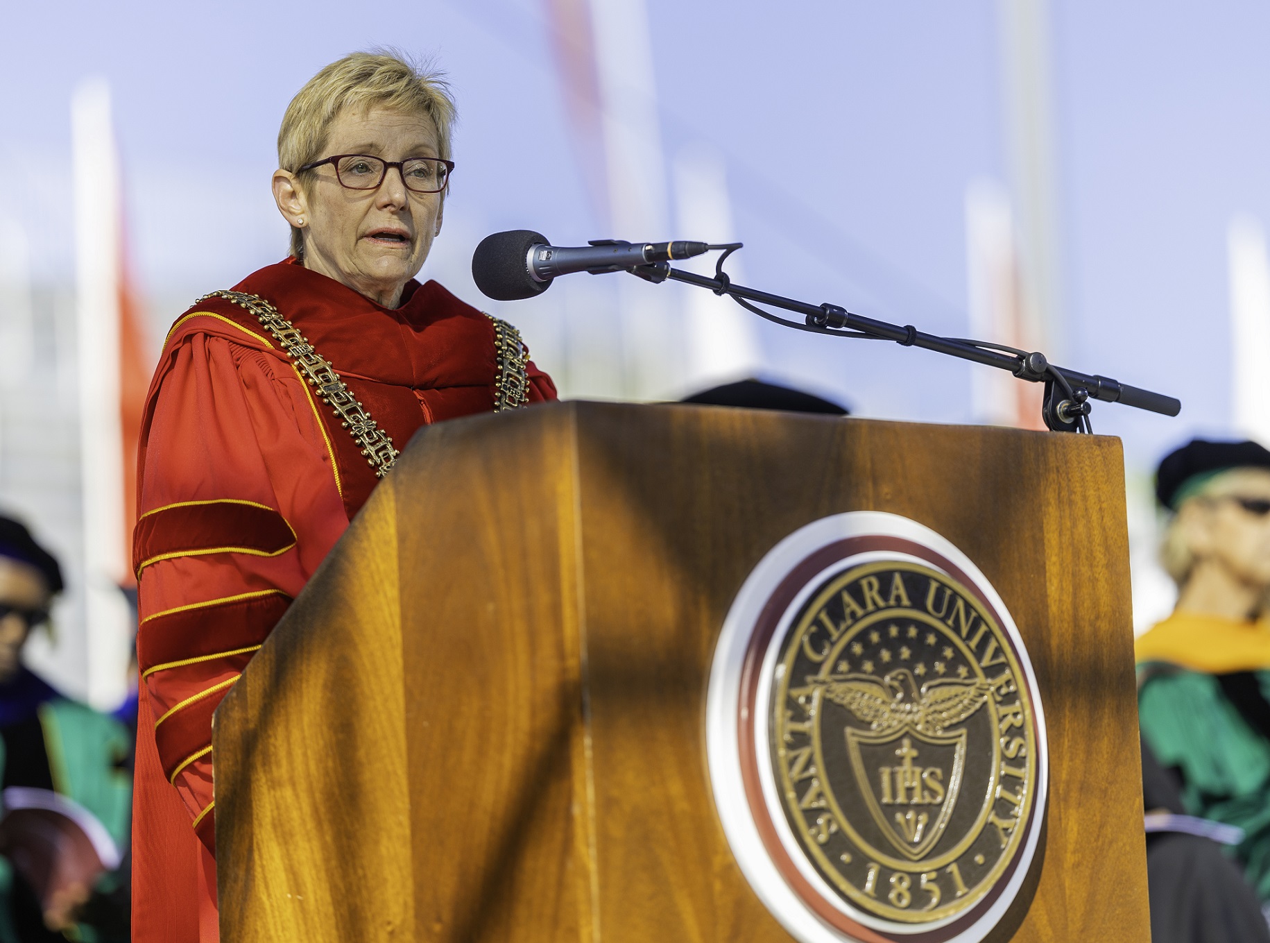 A blonde woman in academic robes at a podium